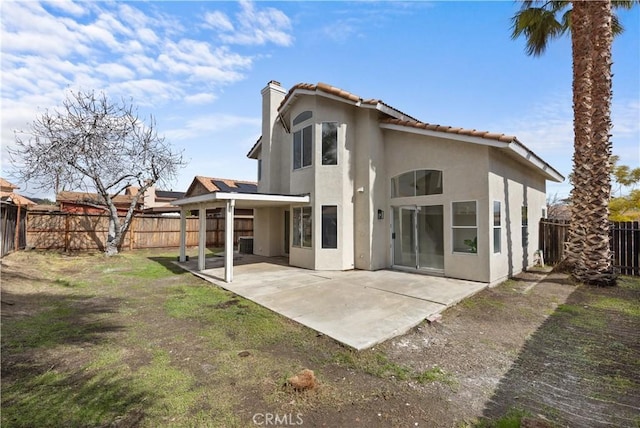 rear view of property featuring a tile roof, a fenced backyard, a chimney, a patio area, and stucco siding