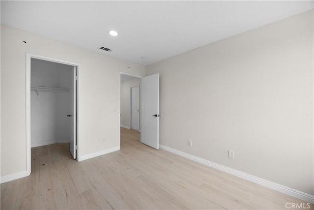 unfurnished bedroom with baseboards, visible vents, a walk in closet, light wood-type flooring, and a closet