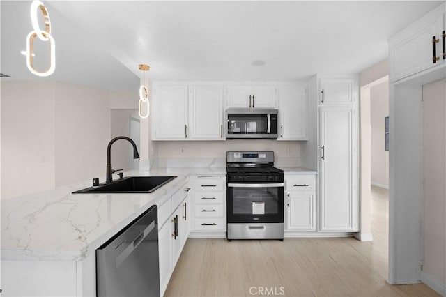 kitchen featuring appliances with stainless steel finishes, white cabinetry, hanging light fixtures, and a sink