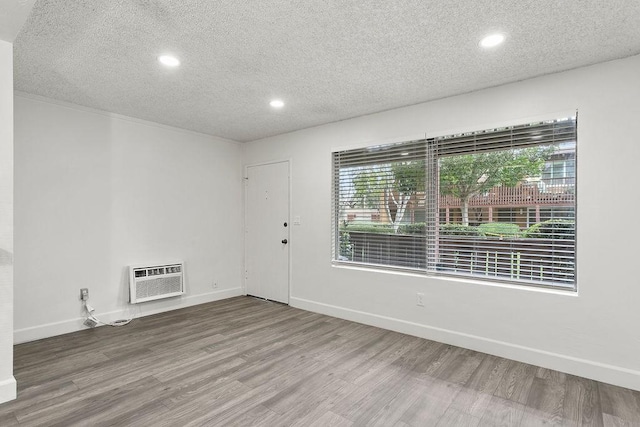 empty room featuring hardwood / wood-style floors, a wall unit AC, and a textured ceiling