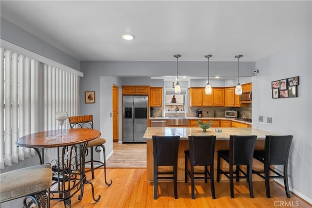 kitchen featuring pendant lighting, sink, a kitchen breakfast bar, stainless steel appliances, and light wood-type flooring