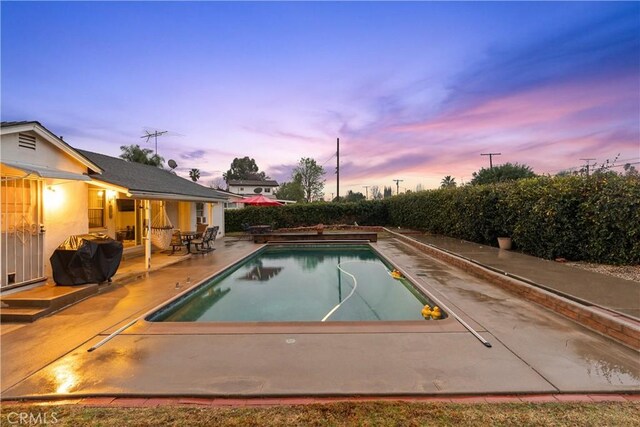 pool at dusk with a grill and a patio area