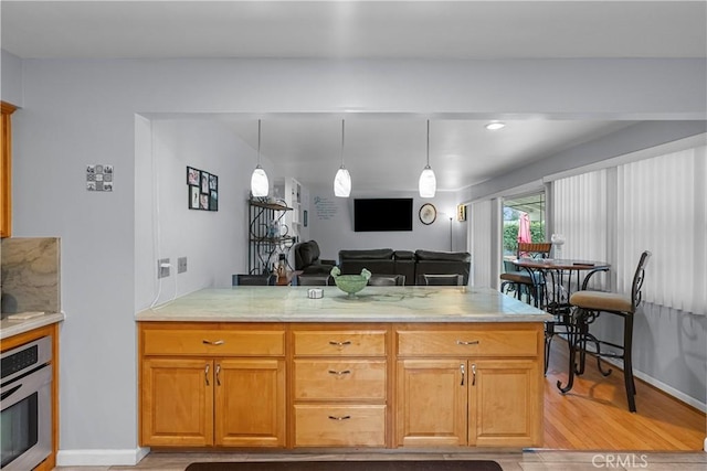 kitchen with stainless steel oven, kitchen peninsula, hanging light fixtures, and light wood-type flooring