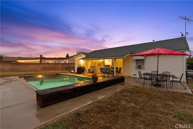 pool at dusk with cooling unit and a patio area