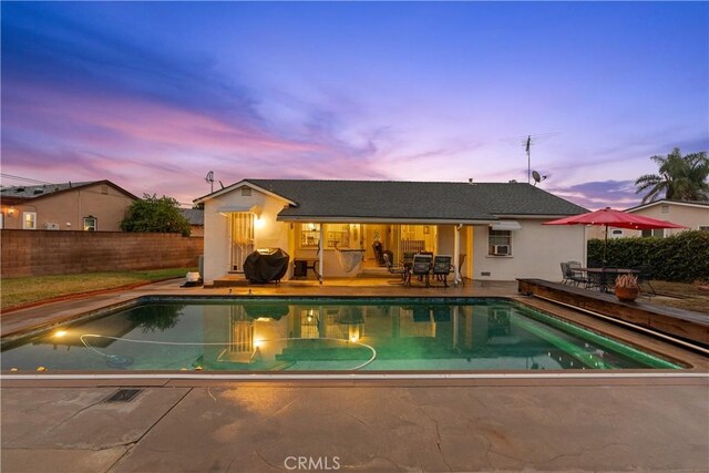 pool at dusk featuring a grill and a patio area