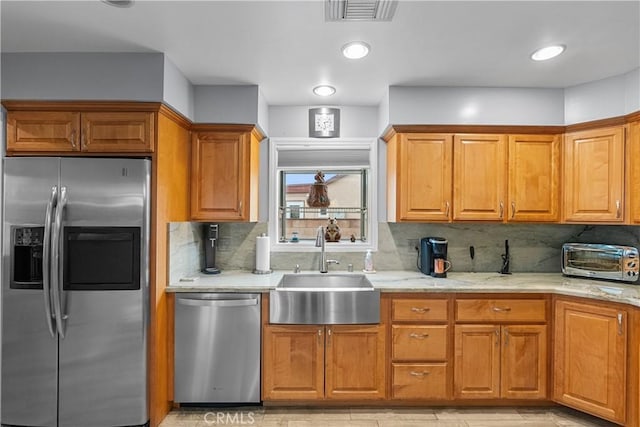 kitchen featuring stainless steel appliances, light stone countertops, sink, and backsplash