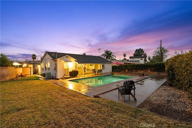 pool at dusk featuring central AC unit, a yard, and a patio area