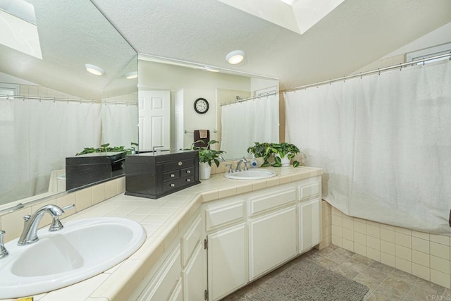 bathroom with vanity, vaulted ceiling with skylight, and a textured ceiling