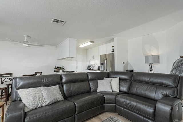 living room featuring ceiling fan, sink, a textured ceiling, and light hardwood / wood-style flooring