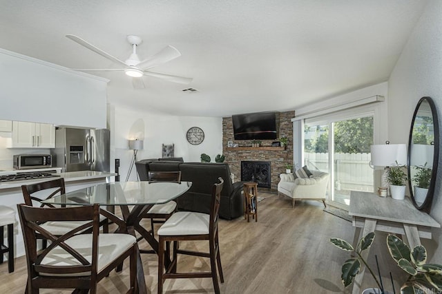 dining room featuring ceiling fan, a stone fireplace, and light hardwood / wood-style floors