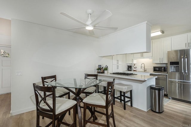 dining area featuring ceiling fan, sink, and light wood-type flooring