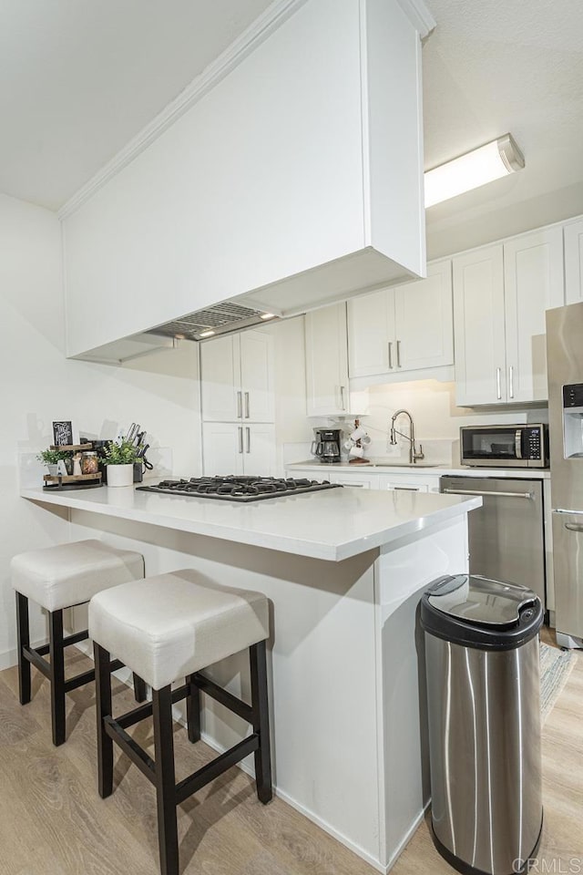 kitchen with appliances with stainless steel finishes, a breakfast bar, white cabinetry, light hardwood / wood-style floors, and kitchen peninsula