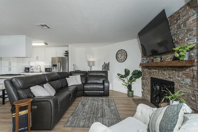 living room with a brick fireplace, wood-type flooring, sink, and a textured ceiling