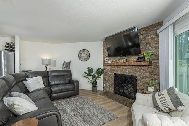 living room featuring a stone fireplace, light hardwood / wood-style flooring, and a textured ceiling