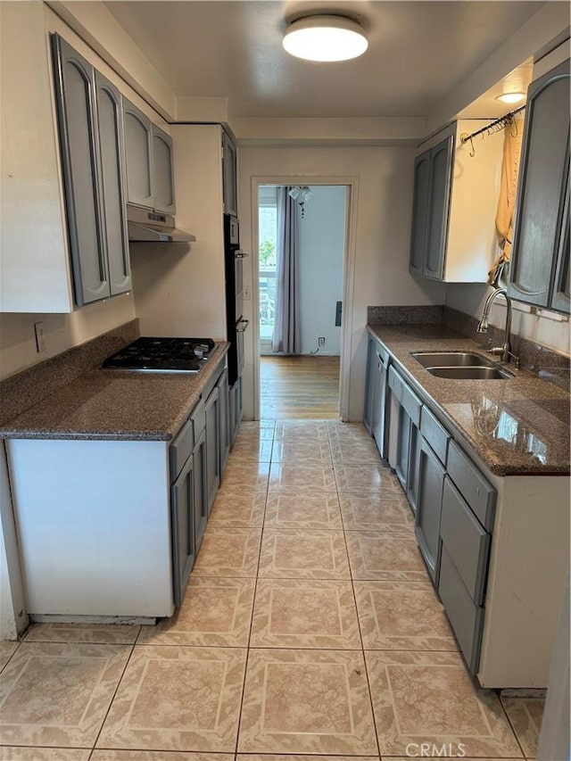 kitchen with under cabinet range hood, double oven, dark stone countertops, gas stovetop, and a sink