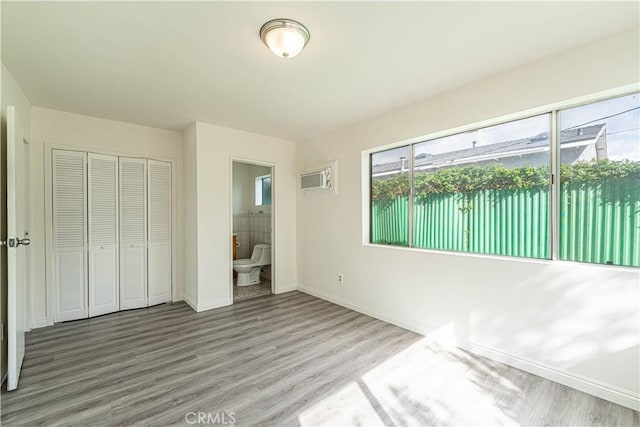 unfurnished bedroom featuring ensuite bathroom, a closet, wood finished floors, and baseboards