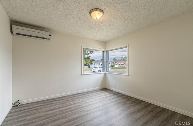 spare room featuring an AC wall unit, a textured ceiling, baseboards, and wood finished floors