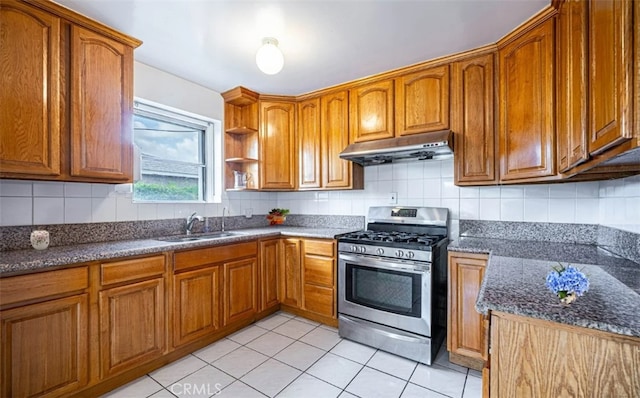 kitchen with brown cabinets, stainless steel gas range, under cabinet range hood, a sink, and light tile patterned flooring