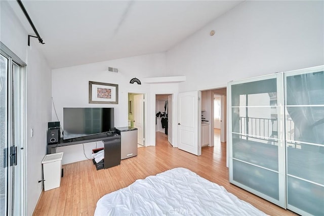 bedroom featuring high vaulted ceiling, a spacious closet, light wood-type flooring, and a closet