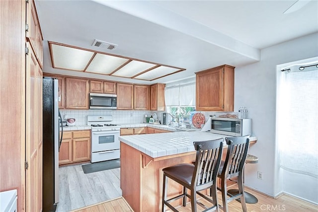 kitchen featuring black fridge, kitchen peninsula, white gas range oven, and light hardwood / wood-style flooring