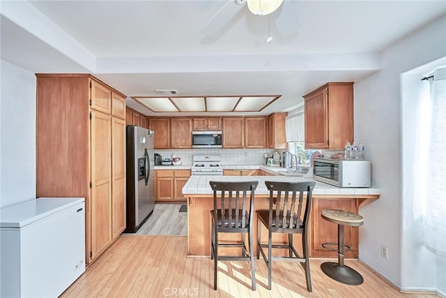 kitchen featuring appliances with stainless steel finishes, a breakfast bar area, light hardwood / wood-style floors, and kitchen peninsula