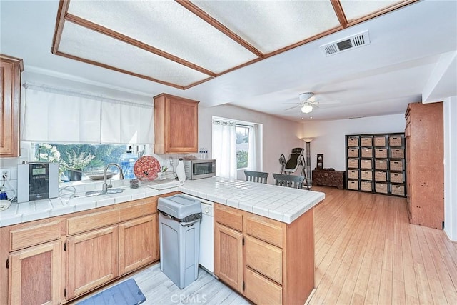 kitchen with light hardwood / wood-style flooring, dishwasher, ceiling fan, tile counters, and kitchen peninsula