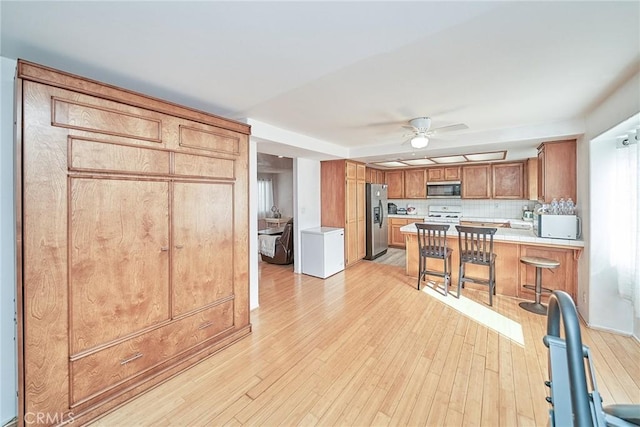 kitchen featuring appliances with stainless steel finishes, light hardwood / wood-style flooring, a kitchen breakfast bar, and kitchen peninsula