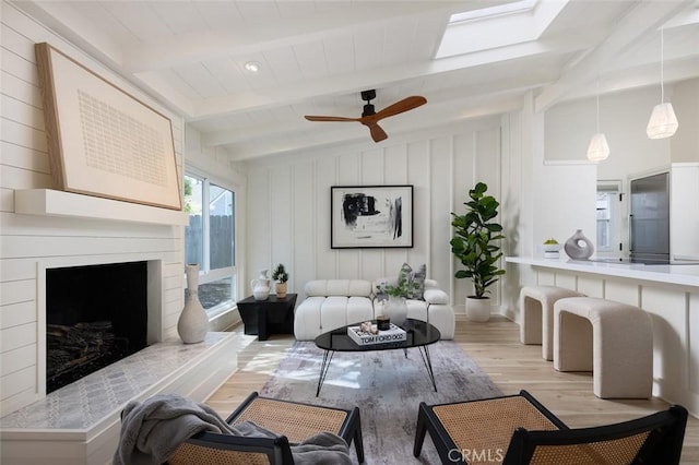 living room with ceiling fan, light hardwood / wood-style flooring, and vaulted ceiling with skylight