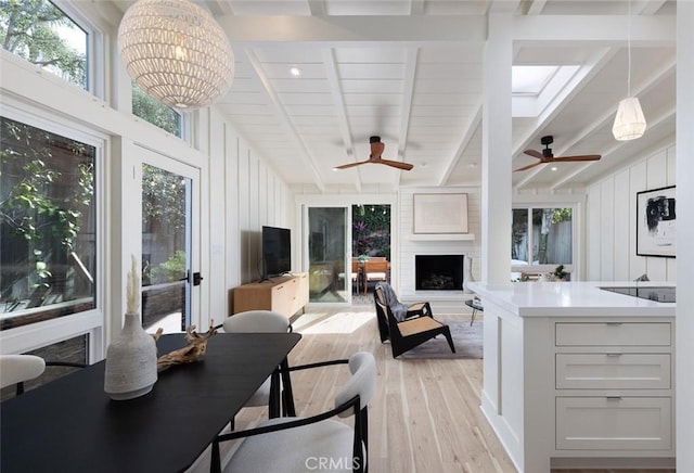 interior space featuring a skylight, light hardwood / wood-style floors, beamed ceiling, a fireplace, and ceiling fan with notable chandelier