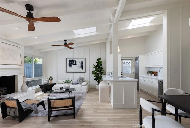 living room with lofted ceiling with skylight, a large fireplace, ceiling fan, and light wood-type flooring