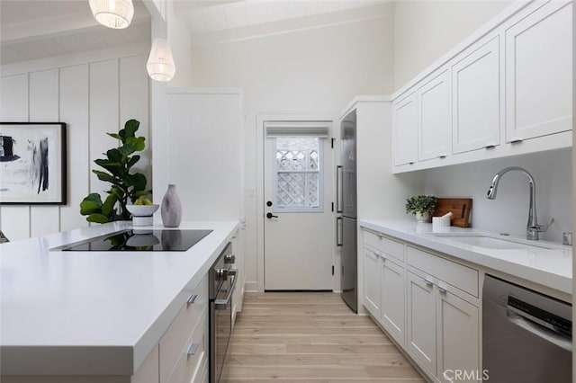 kitchen with pendant lighting, sink, appliances with stainless steel finishes, white cabinetry, and light wood-type flooring