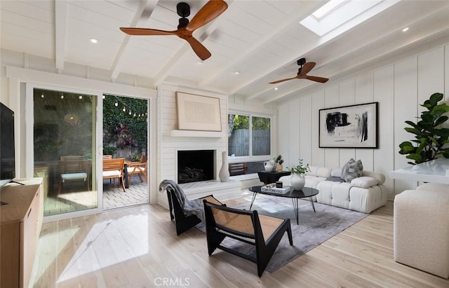 living room with ceiling fan, a large fireplace, lofted ceiling with skylight, and light hardwood / wood-style flooring