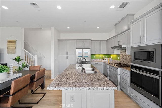 kitchen with an island with sink, built in appliances, sink, and gray cabinetry