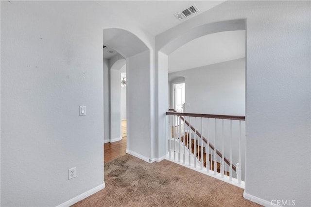 hall with carpet, arched walkways, visible vents, an upstairs landing, and baseboards