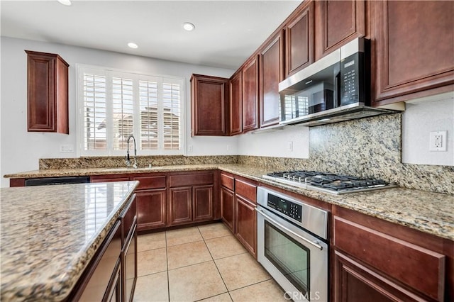 kitchen featuring light tile patterned floors, decorative backsplash, appliances with stainless steel finishes, light stone counters, and a sink