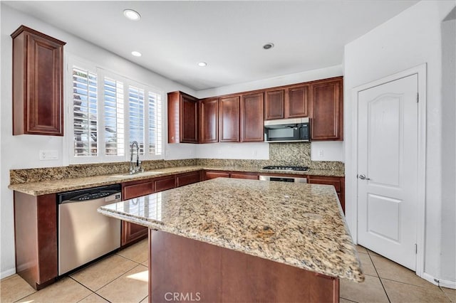 kitchen with appliances with stainless steel finishes, light stone counters, a center island, a sink, and light tile patterned flooring