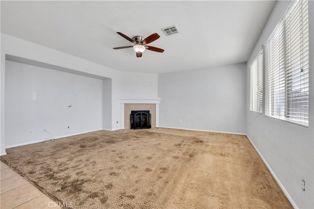 unfurnished living room featuring a tile fireplace, light carpet, visible vents, baseboards, and a ceiling fan