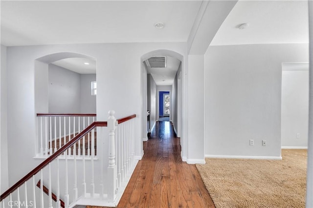 hall featuring baseboards, arched walkways, wood finished floors, and an upstairs landing