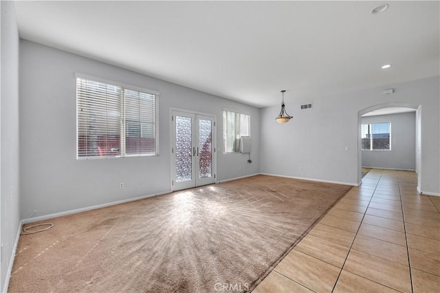 empty room featuring light carpet, visible vents, arched walkways, french doors, and a healthy amount of sunlight