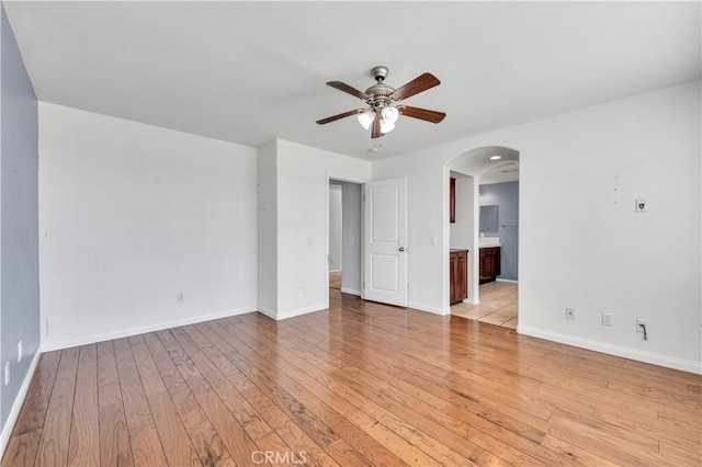 unfurnished room featuring baseboards, light wood-style flooring, arched walkways, and a ceiling fan