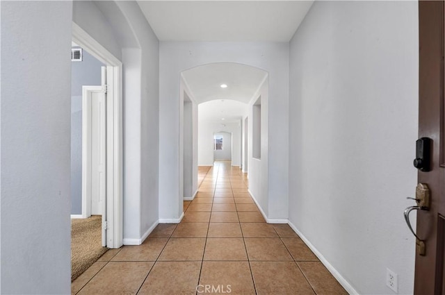 hallway featuring arched walkways, light tile patterned flooring, visible vents, and baseboards