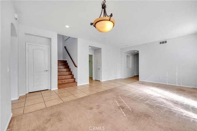 unfurnished room featuring light tile patterned floors, arched walkways, light carpet, visible vents, and stairway