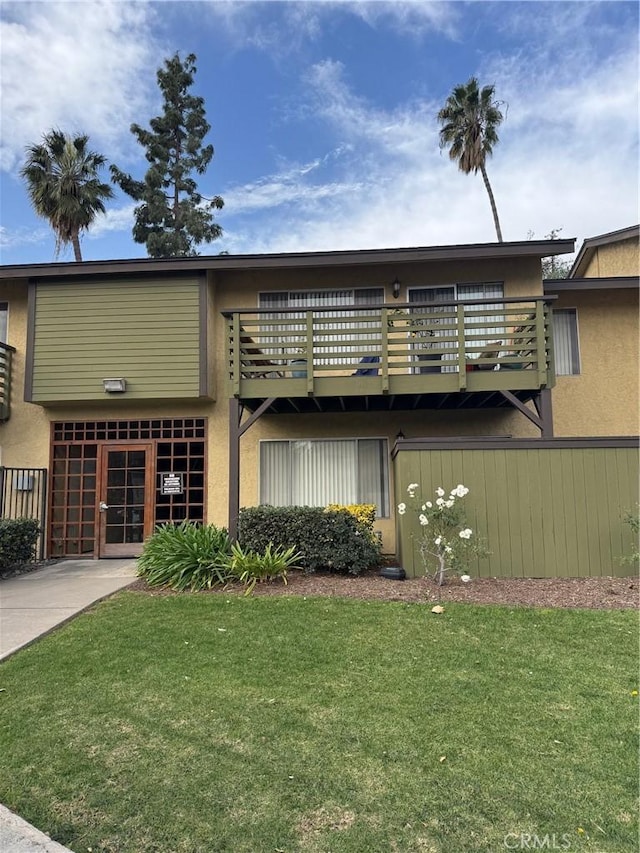 view of front facade with a balcony, a front lawn, and stucco siding