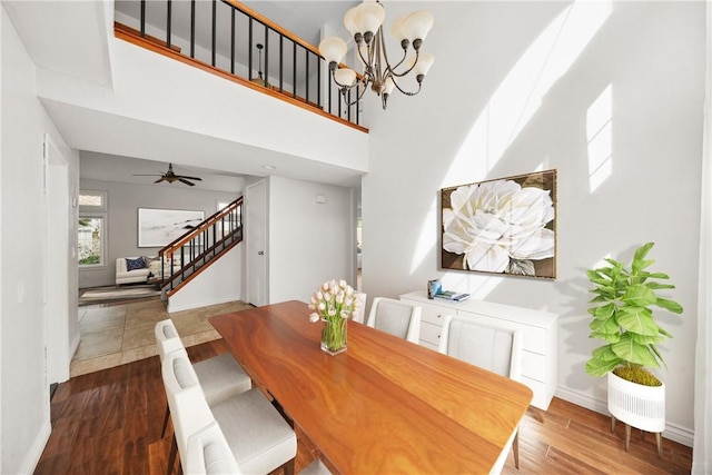 dining room with stairs, ceiling fan with notable chandelier, dark wood finished floors, and baseboards