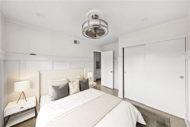 bedroom featuring a wainscoted wall, visible vents, a decorative wall, and a closet