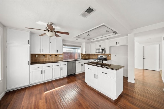 kitchen featuring a center island, stainless steel appliances, dark countertops, visible vents, and white cabinetry