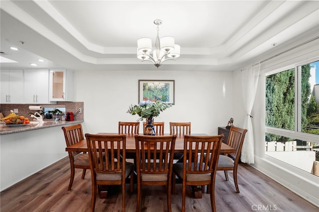 dining space featuring a raised ceiling, wood-type flooring, and a notable chandelier