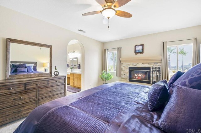 bedroom featuring visible vents, connected bathroom, a stone fireplace, and multiple windows