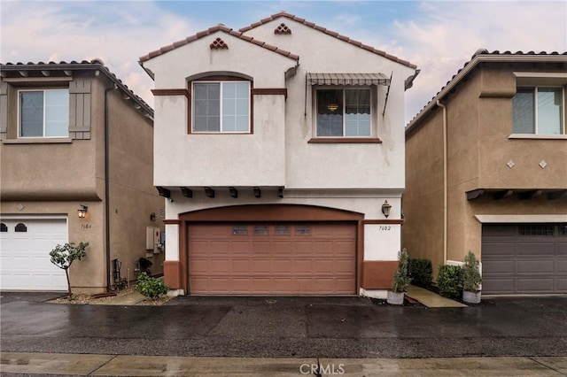 view of front facade with a garage, driveway, a tile roof, and stucco siding