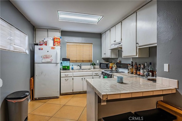 kitchen featuring sink, white appliances, white cabinetry, tile counters, and light tile patterned flooring